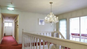A hotel hallway with a red carpet, white railing, and a chandelier. - Pension Ohayo (Hakuba)