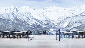 A deck with tables and chairs overlooking snow-covered mountains. - Pension Ohayo (Hakuba)