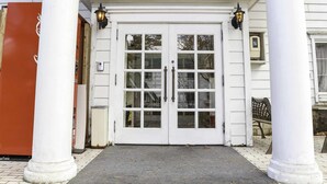 A white building with a double door, two columns, and two wall-mounted lamps. - Pension Ohayo (Hakuba)