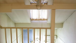 A room with a sloped ceiling, a window with patterned curtains, a wooden railing, and a bed with a floral bedspread. - Pension Ohayo (Hakuba)
