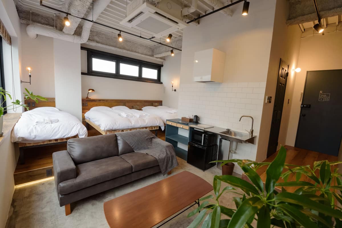 A compact hotel room with two single beds, a sofa, a small kitchenette, and a bathroom.