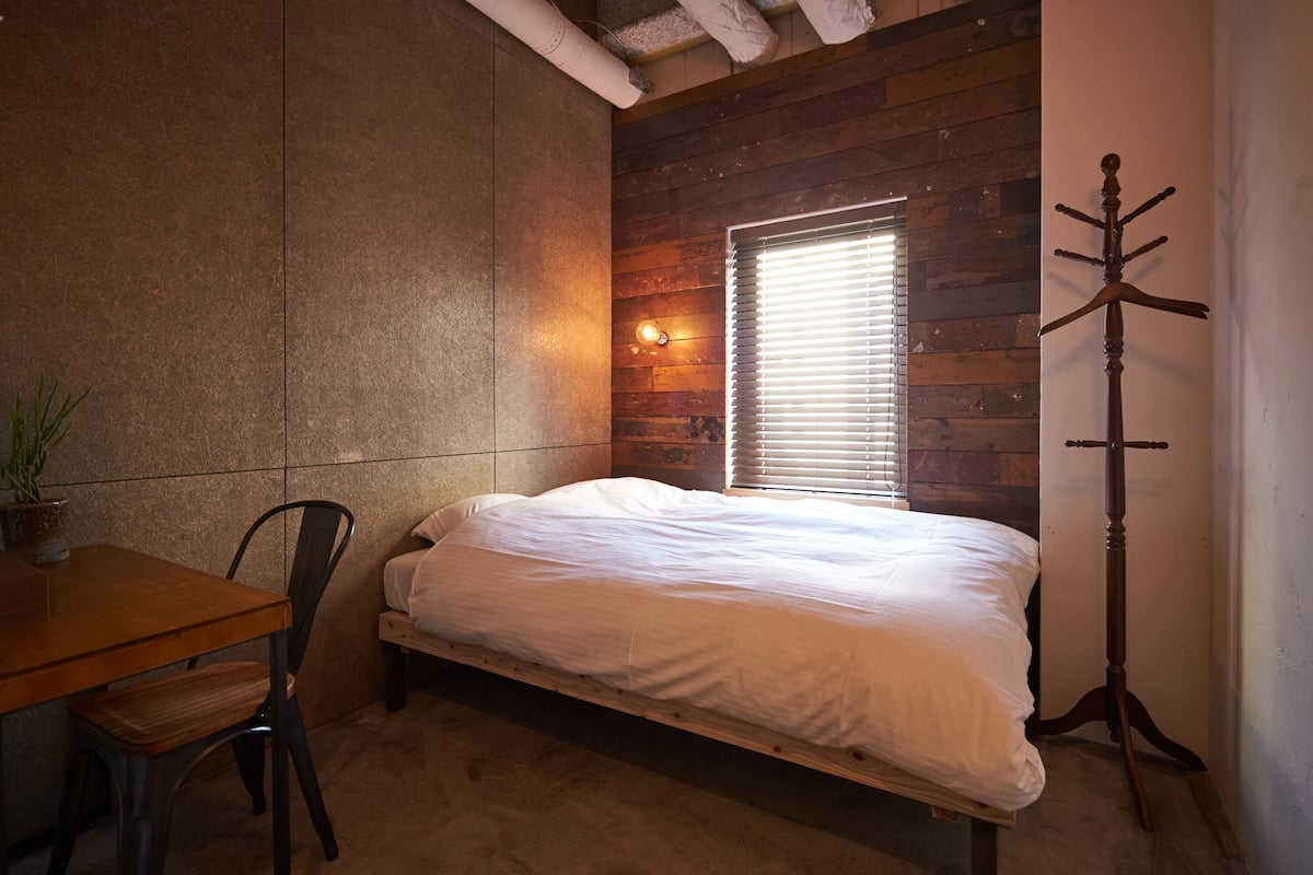 A bedroom with a wooden headboard, a bedside table with a plant, a single bed, and a wooden coat rack.
