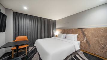 A hotel room with a bed, a desk, an orange chair, and a marble accent wall.