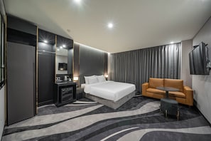 A modern hotel room with a large bed, a sofa, a small table, a desk with a lamp, and a TV mounted on the wall.