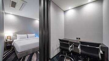 A hotel room with a bed, bedside table, lamp, and a desk with two chairs.