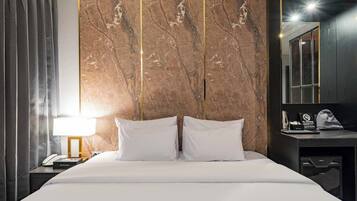 Habitación de hotel con una cama, una mesita de noche con lámpara, un escritorio con teléfono y un espejo.