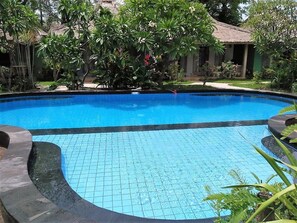 A swimming pool with tiled edges, surrounded by lush greenery and a thatched-roof structure. - Mahaputri Bungalow (Gili Trawangan)