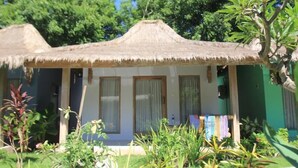 Ein Bungalow mit einem Reetdach, einer kleinen Veranda und einem Garten mit verschiedenen Pflanzen.