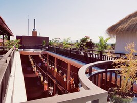 Un espace extérieur à plusieurs niveaux, doté d’un balcon incurvé, de plantes en pot et de décorations suspendues.