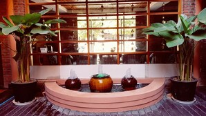 A fountain with three tiers, surrounded by potted plants, in front of a window with a grid pattern. - Bagan View Hotel (Nyaung-U)