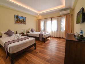 A hotel room with two beds, wooden flooring, a desk with a water bottle, and a painting on the wall. - Bagan View Hotel (Nyaung-U)