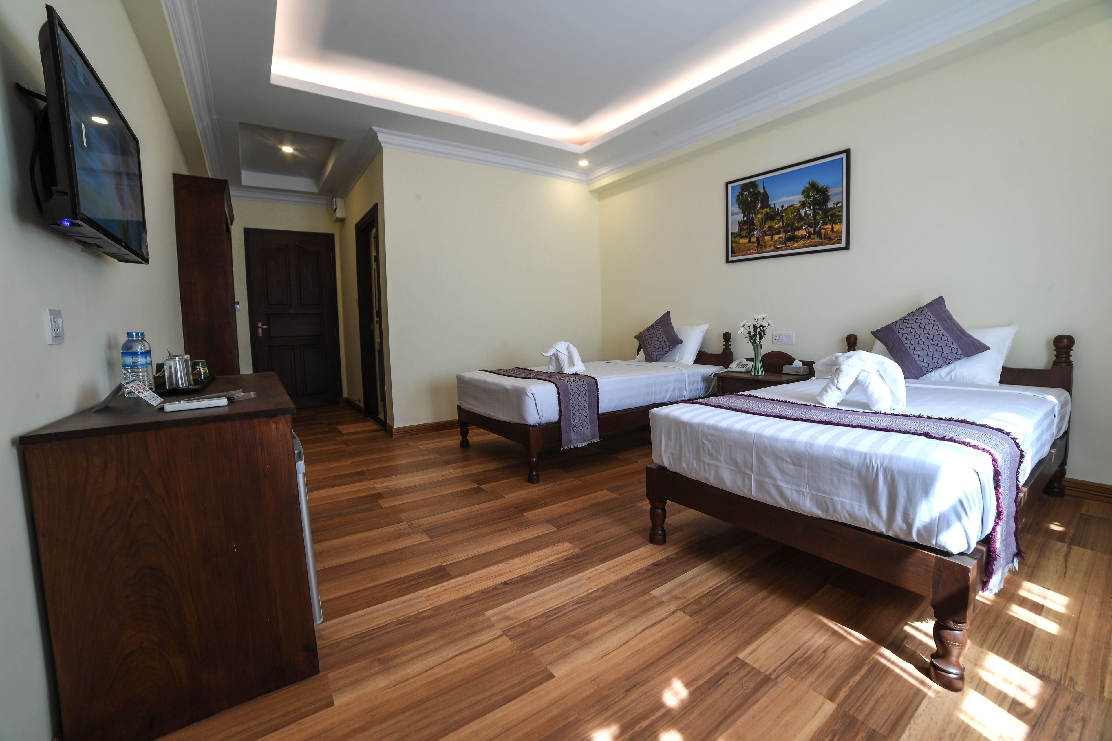 A hotel room with two beds, a wooden desk, a flat-screen TV, and a painting on the wall.