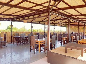 An outdoor covered patio with multiple tables and chairs, a wooden fence, and a clear view of the surrounding greenery. - Bagan View Hotel (Nyaung-U)