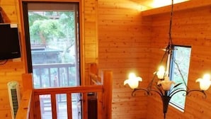 Une cabane en bois avec une chambre à coucher située en mezzanine, un escalier et un lustre.
