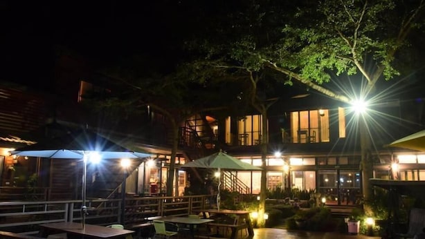 Un espace extérieur aménagé en terrasse, avec des tables et des chaises, entouré d’une plateforme en bois et d’arbres.