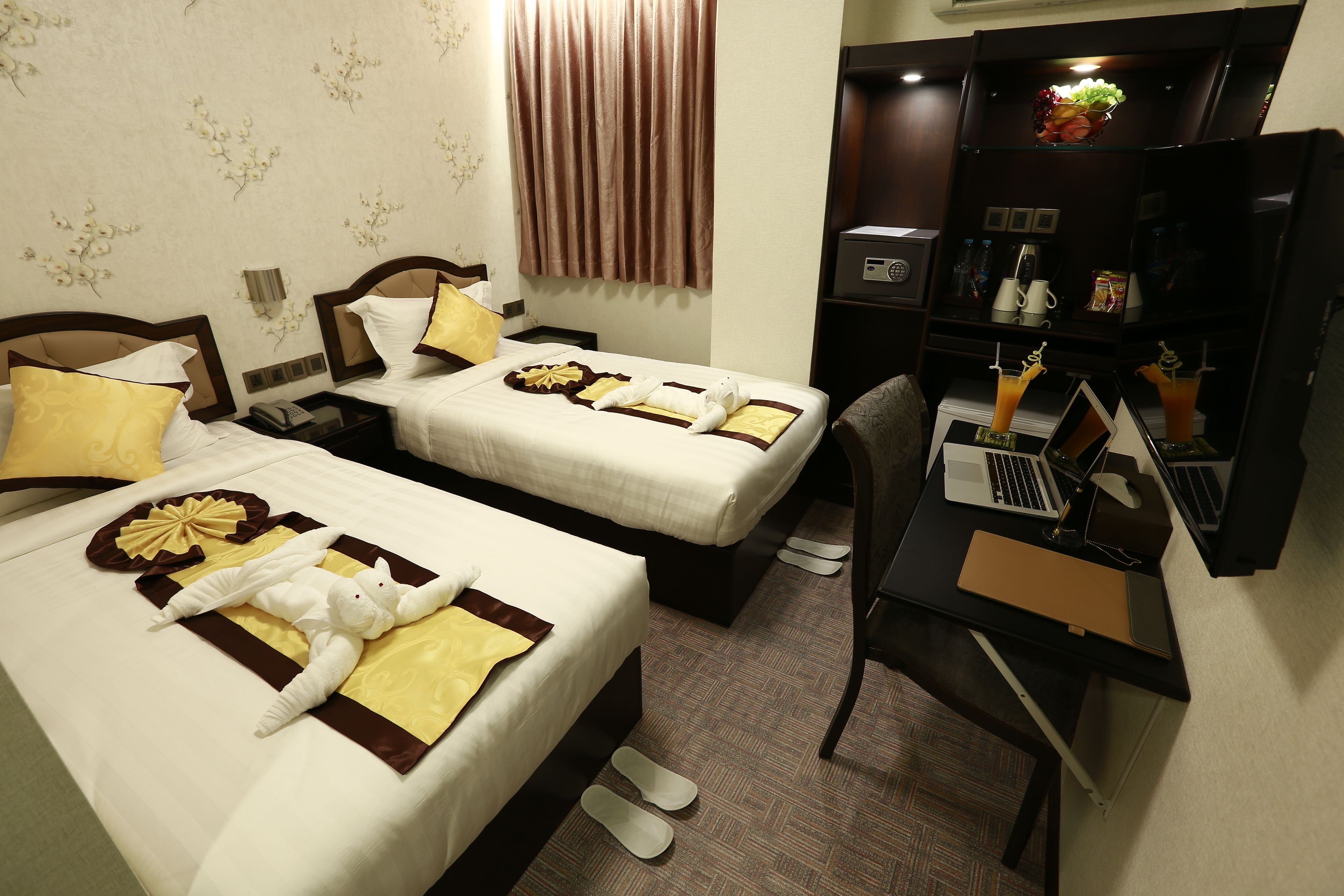 Een hotelkamer met twee bedden, elk met handdoeken en kussens, een bureau met een laptop en een minibar.