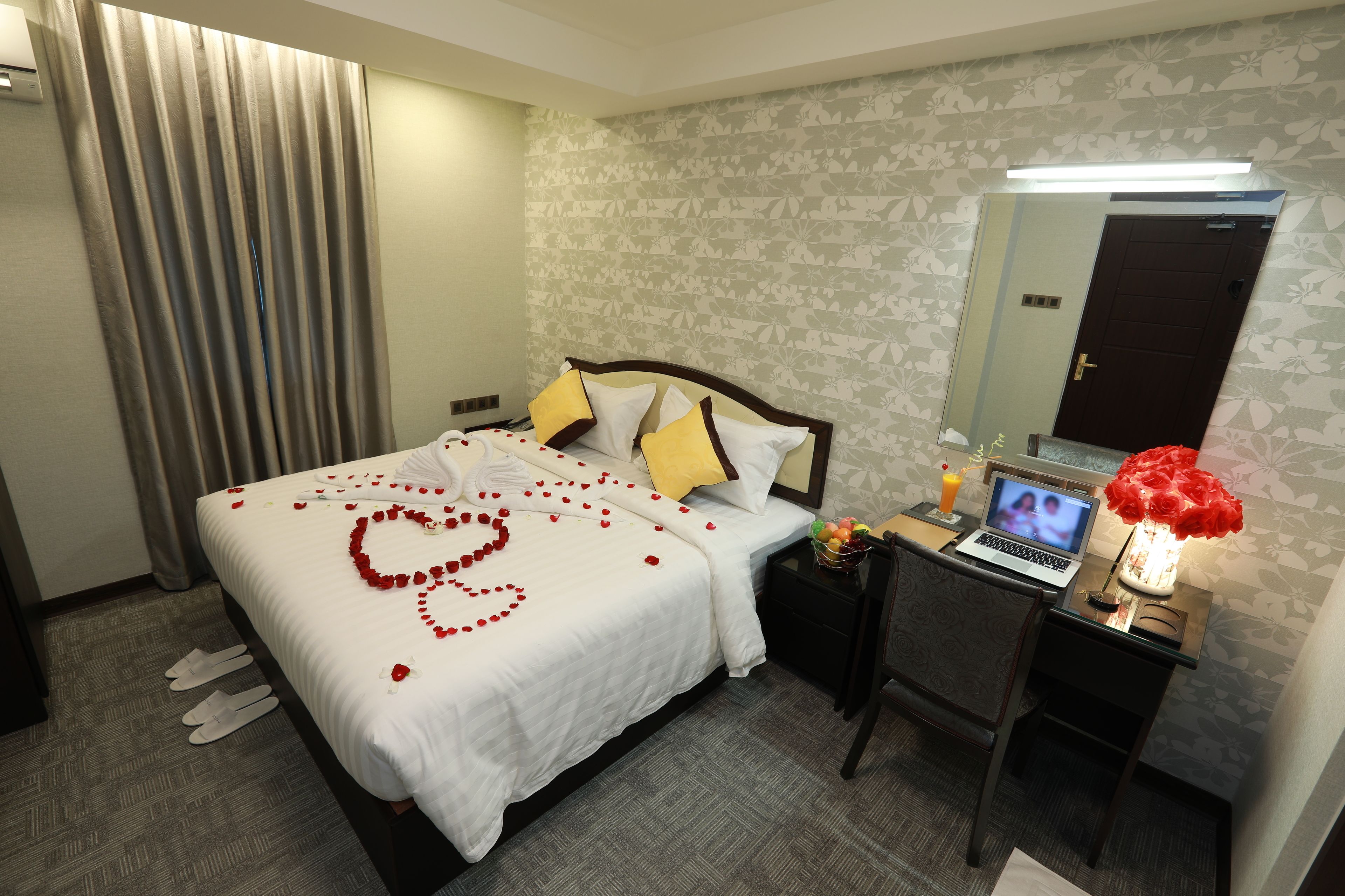 Habitación de hotel con una cama bien tendida, una computadora portátil sobre una mesita de noche y un espejo que refleja la habitación.