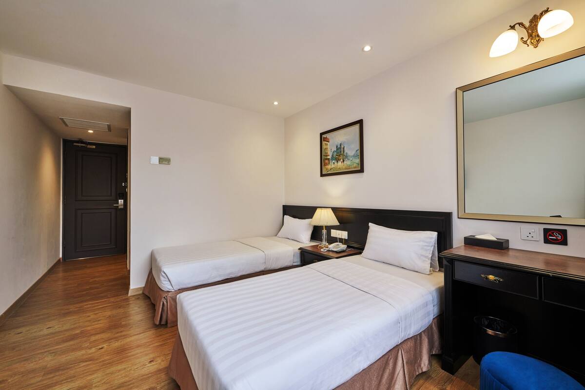 Une chambre d’hôtel avec deux lits, un bureau, une chaise, une lampe, un tableau et un miroir.