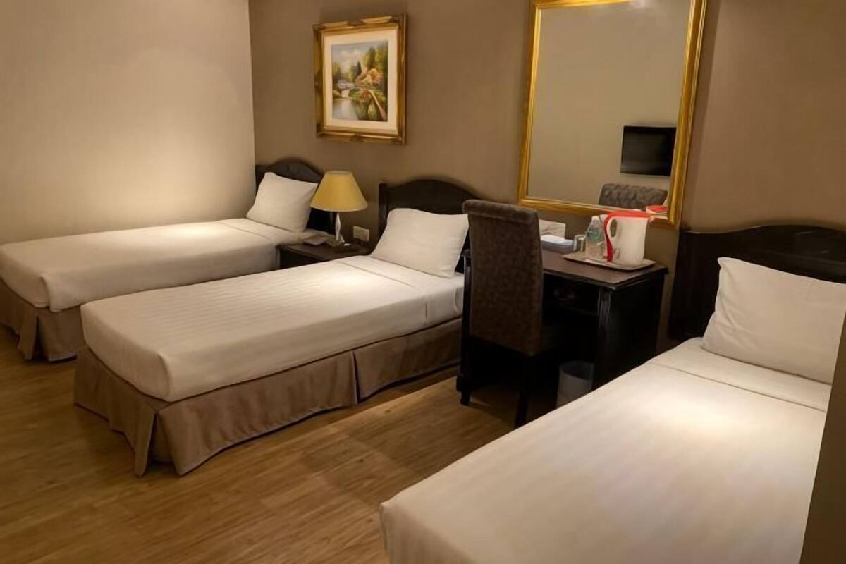 Une chambre d’hôtel avec deux lits simples, un bureau avec une chaise, une lampe et un téléviseur.