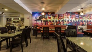 Un restaurante con una decoración moderna, que ofrece una variedad de opciones de asientos, como mesas y cabinas, un mural colorido en la pared de fondo, e iluminación colgante.