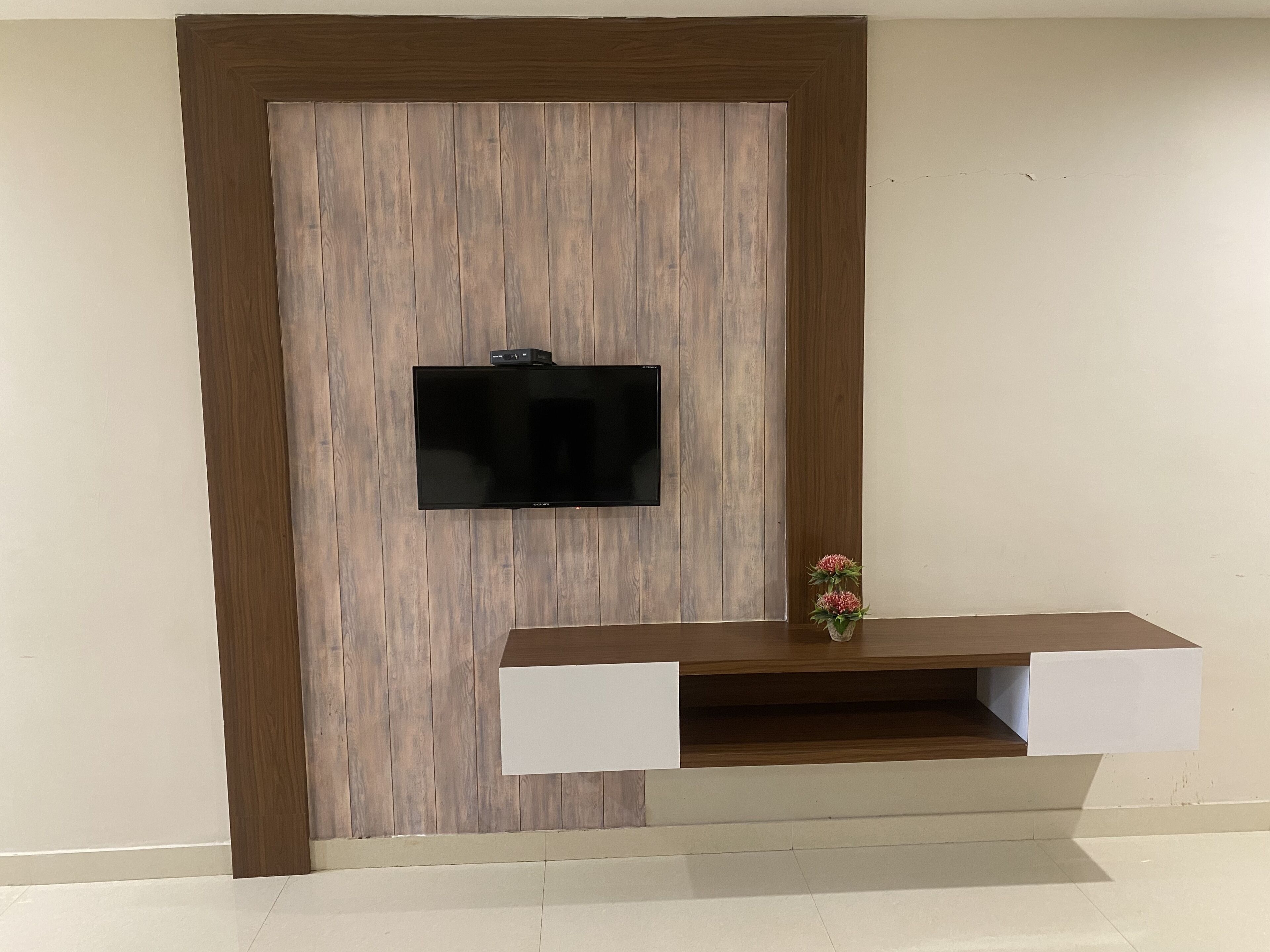 A wall-mounted TV with a wooden panel design and a small shelf below it.