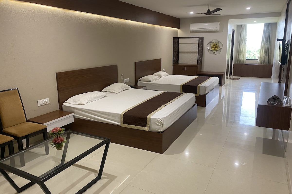 A hotel room with two beds, a glass coffee table, a chair, and a desk with a mirror.