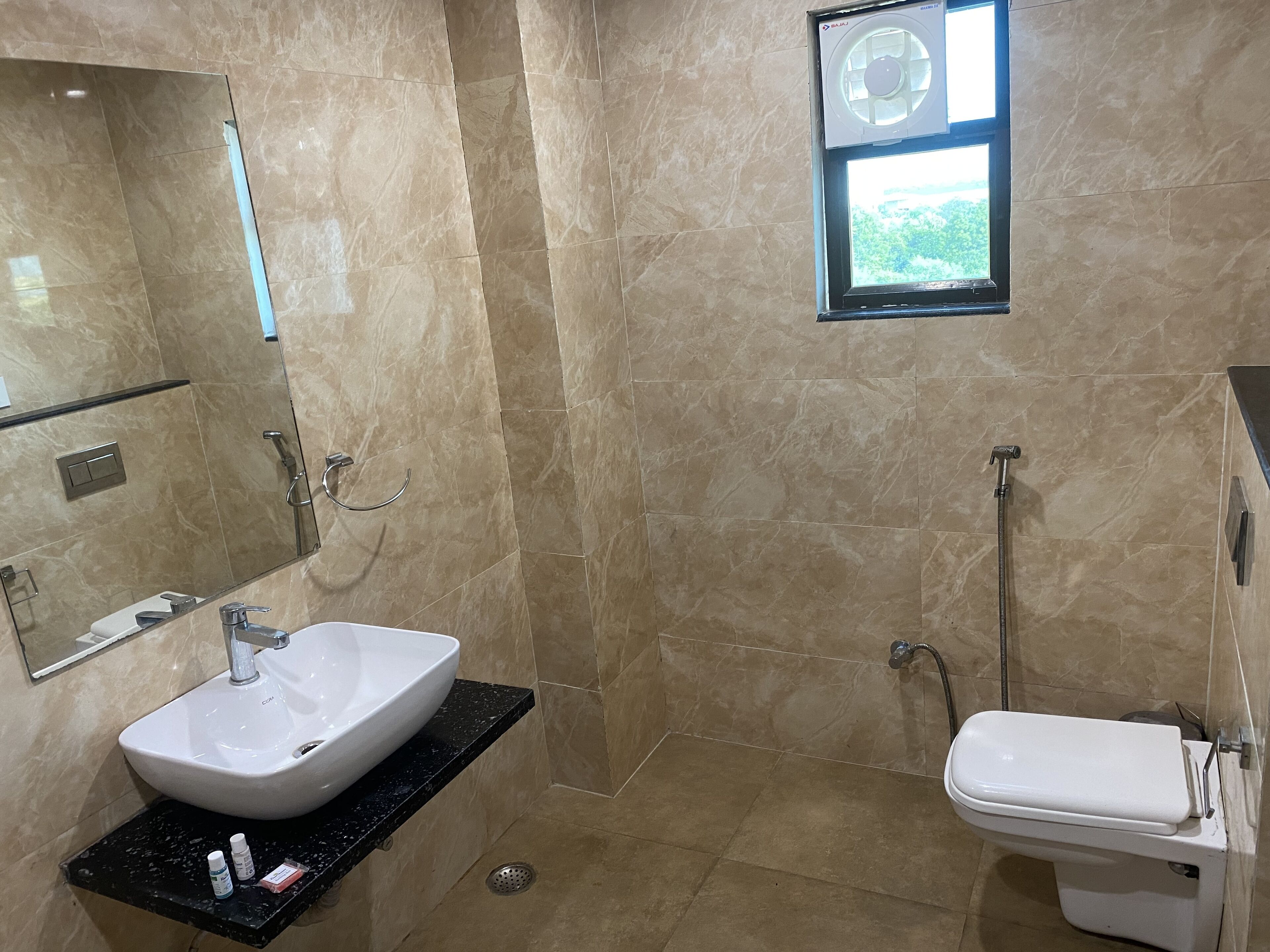 A bathroom with a white sink, a toilet, a shower, and a window with a view of greenery.