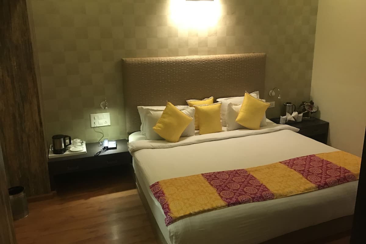A neatly made bed with a patterned throw, a bedside table with a lamp, and a wall-mounted light fixture.