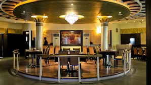 Ein Restaurant mit einem runden Tisch in der Mitte, umgeben von Stühlen, einer Kandelaber und einem großen Gemälde an der Wand.