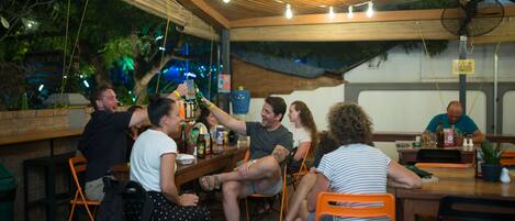A group of people seated at a wooden table in an outdoor setting with string lights overhead.