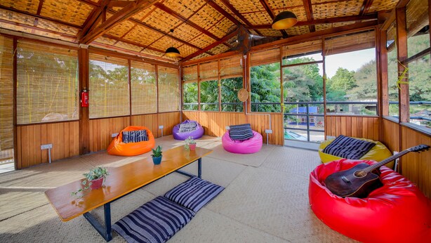 Una habitación con techo de madera, ventanas amplias y una mesa con cojines y una guitarra.