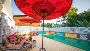Zona de piscina con sillas reclinables y sombrillas, piscina y valla con marcas.