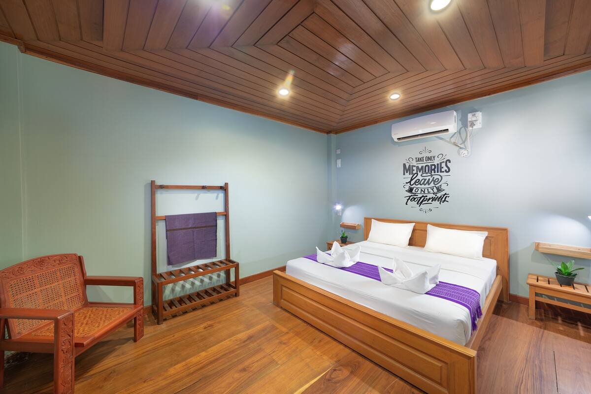 Une chambre à coucher avec un lit en bois, une chaise en bois, une petite table et un climatiseur fixé au mur.
