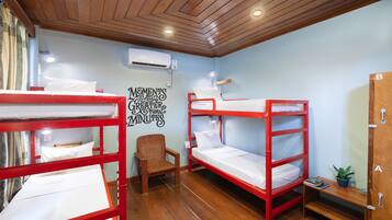 A dormitory room with bunk beds, a wooden chair, a small table with a plant, and a wall-mounted air conditioner.