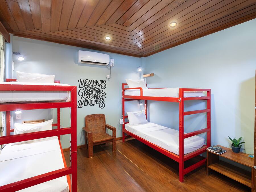 A dormitory room with bunk beds, a wooden chair, a small table with a plant, and a wall-mounted air conditioner.