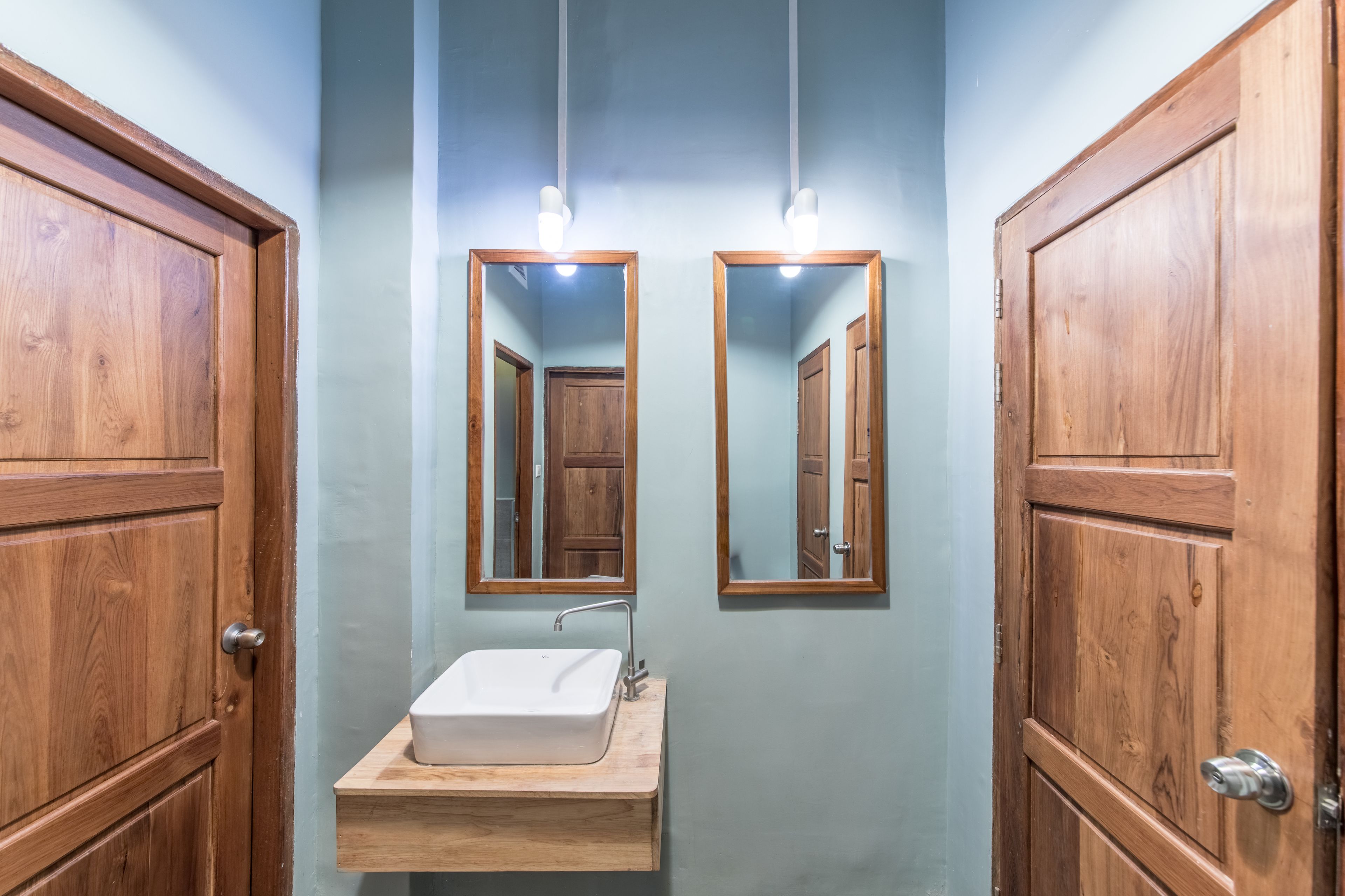 Un baño con puertas de madera, un lavabo blanco y dos espejos colocados en la pared.