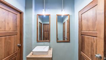 Un baño con puertas de madera, un lavabo blanco y dos espejos colocados en la pared.