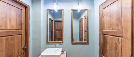 A bathroom with wooden doors, a white sink, and two mirrors mounted on the wall.
