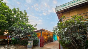 Un restaurante llamado Ostello Bello con un área de estar al aire libre cubierta, rodeado de exuberante vegetación.