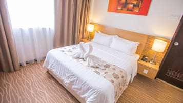 A hotel room with a large bed, two bedside lamps, a headboard, and a painting on the wall.