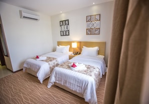A hotel room with two beds, a nightstand, a lamp, and artwork on the walls.