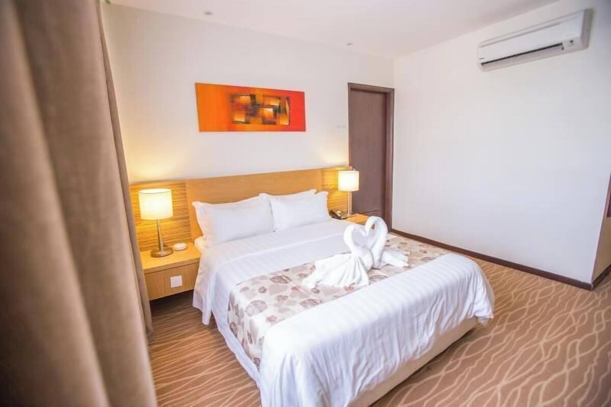 A hotel room with a bed, two bedside lamps, a wall-mounted air conditioner, and a door.