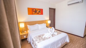A hotel room with a large bed, two bedside lamps, a wall-mounted air conditioner, and a door. - VIP Hotel Segamat (Segamat)