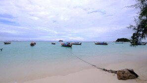 Ein Strand mit mehreren vor Anker liegenden Booten in ruhigem Wasser, einem sandigen Ufer und einer entfernten Insel.