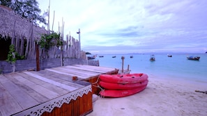 A wooden deck with a thatched roof, a red inflatable raft, and boats in the water. - Captain Yut's Bungalow (Koh Lipe)