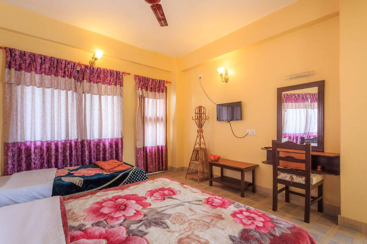 A bedroom with two beds, a desk, a chair, a television, and a mirror.