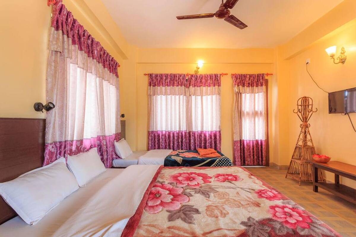 A hotel room with two beds, a ceiling fan, a TV, and a window with curtains.
