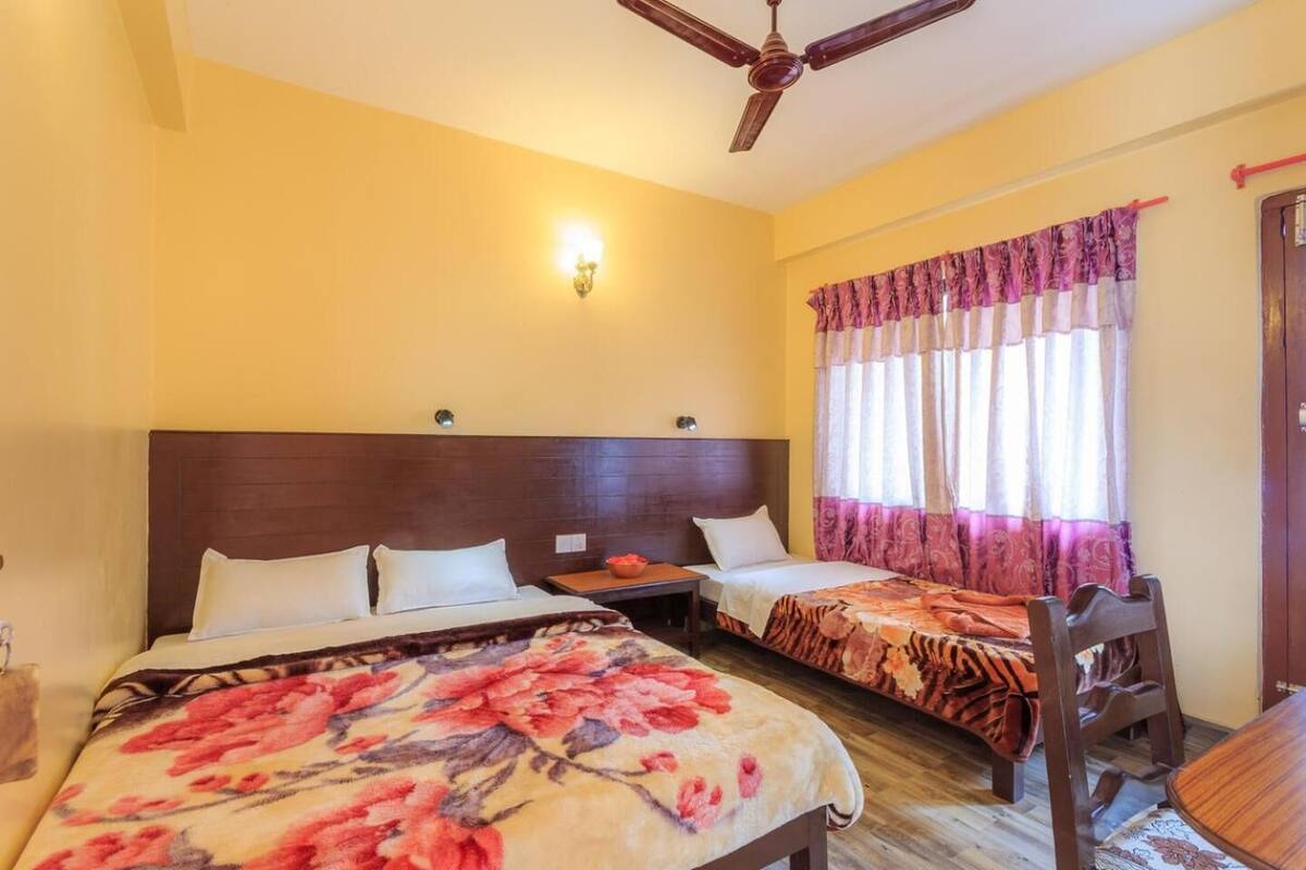 A hotel room with two beds, a wooden headboard, a ceiling fan, a nightstand, a table, and a chair.