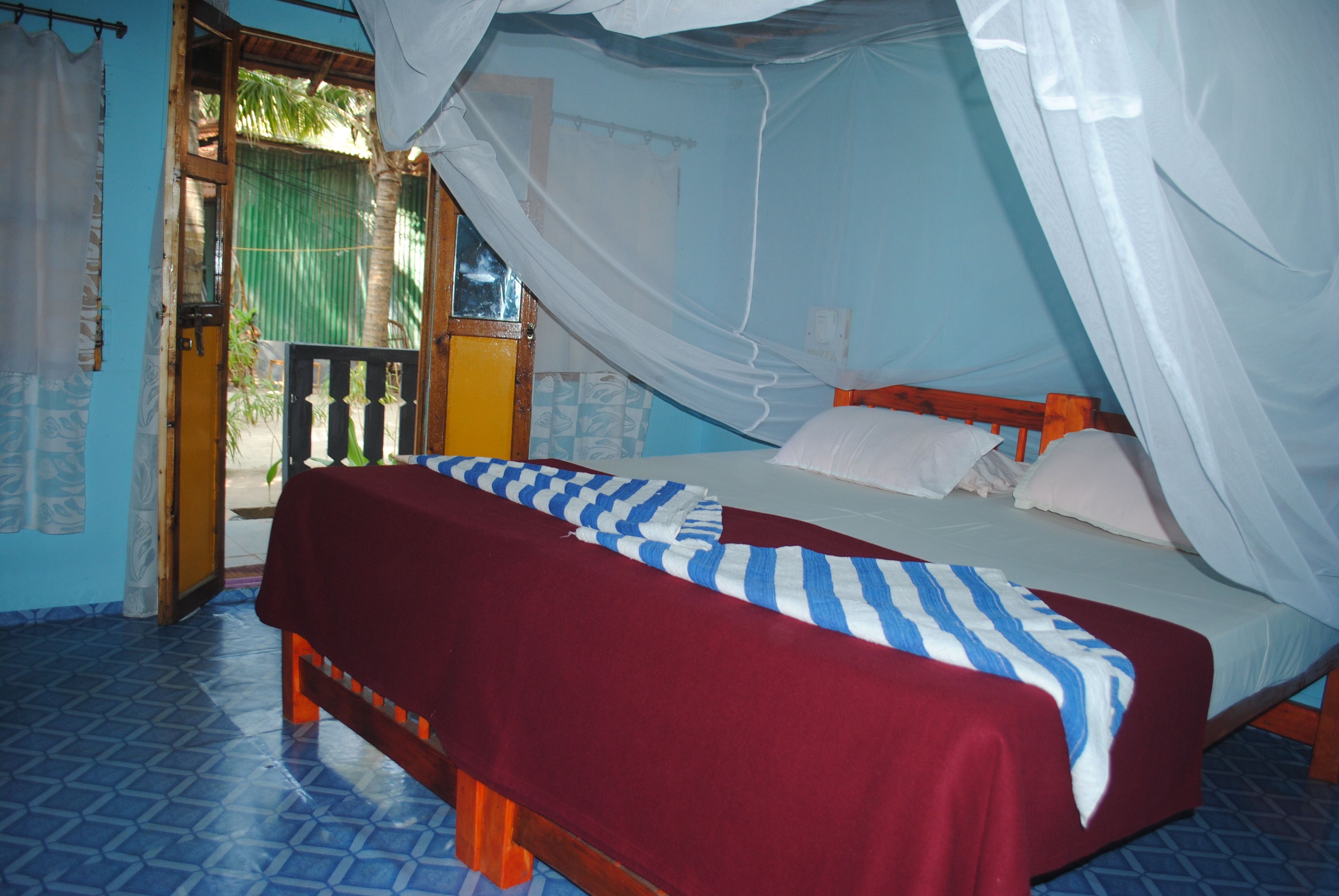 A room with a bed, a bench, and a door leading outside.