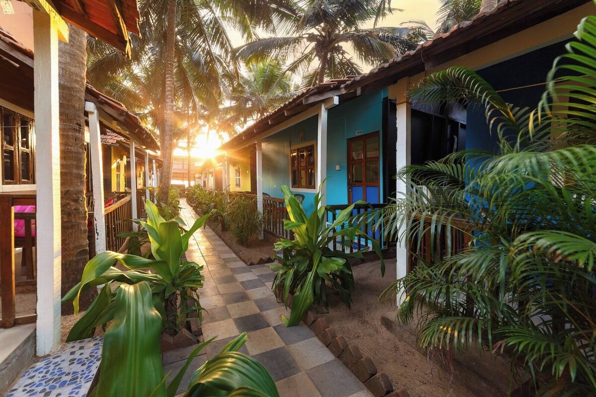 A pathway leading to a building with a checkered floor, surrounded by lush greenery and palm trees.